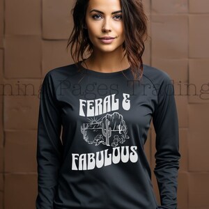 May include: Black long-sleeve shirt with a white graphic print of a desert scene and the text "Feral & Fabulous".