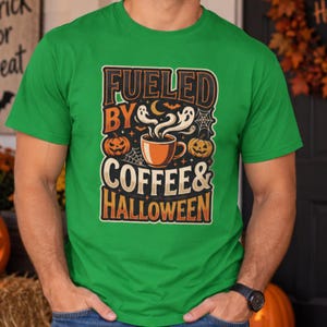 May include: A bright green short-sleeve t-shirt featuring a graphic print with the text FUELED BY COFFEE & HALLOWEEN. The design includes an orange coffee mug with steam, two jack-o'-lanterns, spider webs, a crescent moon, and a small bat.