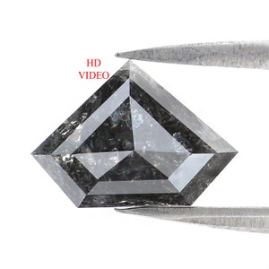 Peut inclure: Un diamant taillé en forme de cerf-volant, de couleur grise, maintenu par une pince. Le diamant présente des inclusions internes et un motif géométrique. Le texte "HD VIDEO" est visible en rouge.