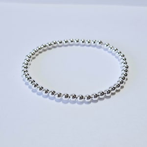 May include: A silver beaded bracelet with a simple design. The bracelet is made of small, round beads that are strung together on a thin cord.