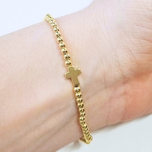 May include: A gold beaded bracelet with a small gold cross charm.