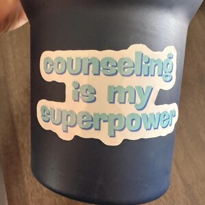 May include: A blue and white sticker on a dark blue tumbler that says "Counseling is my superpower".