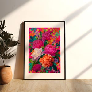 Op de afbeelding: Een ingelijste kunstdruk met een levendig boeket pioenrozen in roze, oranje en witte tinten tegen een geblokte roze en gouden achtergrond. Het kunstwerk wordt gepresenteerd in een zwarte lijst, wat de kleurrijke compositie versterkt.