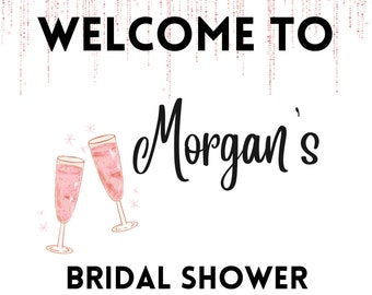 May include: A white sign with the words "WELCOME TO Morgan's BRIDAL SHOWER" in black text. Two champagne flutes with pink liquid are illustrated below the text. The date "04.24.22" is at the bottom. A pink glitter design is at the top.