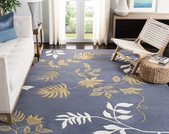 Può includere: Un tappeto blu con un motivo floreale bianco e oro. Il tappeto presenta un motivo ripetuto di foglie e viti, creando un aspetto naturale ed elegante. Il tappeto si trova in un soggiorno.