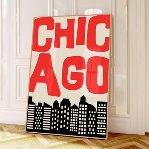 Może przedstawiać: Oprawiony wydruk z napisem "CHICAGO" w czerwonych literach na kremowym tle. Czarno-biała sylwetka panoramy miasta u dołu. Grafika opiera się o białą ścianę.