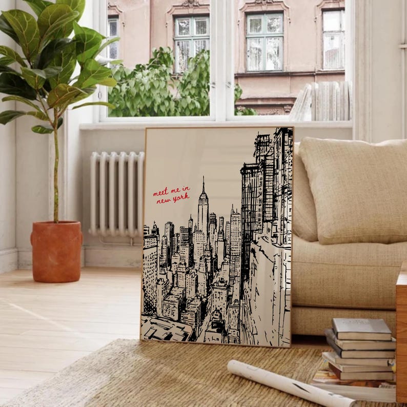 May include: A framed art print featuring a black and white illustration of the New York City skyline. The artwork includes the Empire State Building and other iconic skyscrapers. The phrase "meet me in new york" is written in red script.
