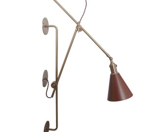 May include: A brass wall-mounted light fixture with a brown leather cone shade. The light has a flexible arm and can be adjusted to different angles.