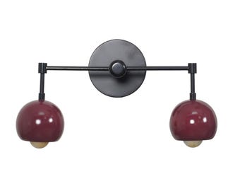May include: Black wall sconce with two red globe-shaped light fixtures. The sconce has a round metal base and two adjustable arms.