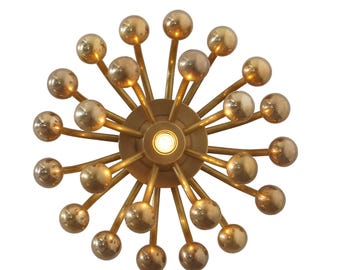 May include: A gold-toned metal ceiling light fixture with a circular base and multiple arms extending outwards. Each arm ends in a round, gold-toned bulb. The light fixture has a modern, geometric design.