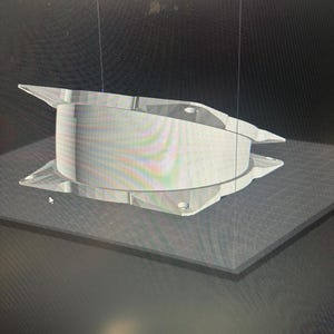 Op de afbeelding: Een helder, geometrisch object met een cilindrisch midden en hoekige uitbreidingen. Het object lijkt gemaakt te zijn van een doorschijnend materiaal, mogelijk plastic of acryl. Het staat op een donkere ondergrond, met een zichtbaar rasterpatroon.