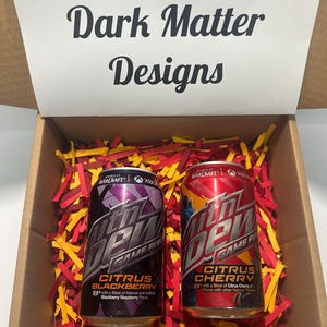 May include: Two cans of Mountain Dew Game Fuel, one citrus blackberry and one citrus cherry, in a brown box with red and yellow shredded paper.