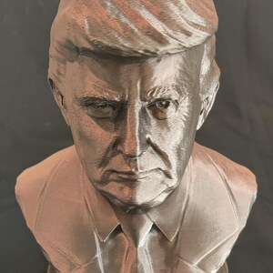 May include: A bronze bust of Donald Trump with the word "TRUMP" inscribed on the base.