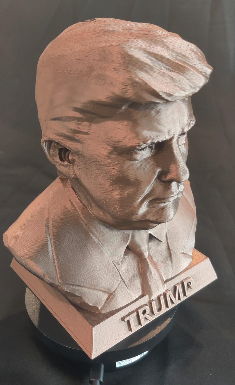 May include: A brown 3D printed bust of a person with the word "TRUMP" printed on the base.