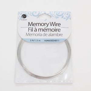 May include: A package of silver-colored memory wire for jewelry making. The label reads "Memory Wire" in English, French, and Spanish. The package contains 5 ft / 1.5 m of wire.