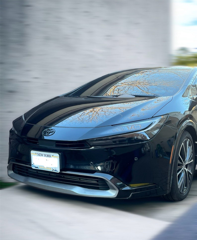 May include: A black Toyota Prius car with a New York license plate. The car has a silver front bumper and black wheels. The car is parked outside on a sunny day.