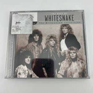 Puede incluir: Una caja de CD con el álbum "The Best of Whitesnake: The Millennium Collection". La portada muestra una fotografía en tonos sepia de los miembros de la banda. La caja del CD está en una funda de plástico transparente.