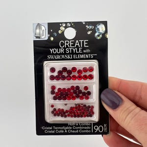 May include: A package of red Swarovski Elements hotfix crystals. The package has three compartments filled with various sizes of red crystals. The package reads "CREATE YOUR STYLE with SWAROVSKI ELEMENTS".