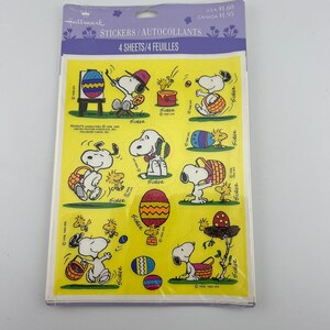 May include: A package of Hallmark stickers featuring Snoopy and Woodstock celebrating Easter. The stickers are on a yellow background and include images of Snoopy painting eggs, carrying baskets, and other Easter-themed activities. The package reads "STICKERS/AUTOCOLLANTS".
