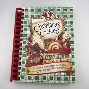 May include: A spiral-bound cookbook titled Christmas Cookies by Gooseberry Patch. The cover features illustrations of various cookies, a red ornament, and green plaid patterns. Text includes A collection of incredibly edible cookies, plus nifty packaging.