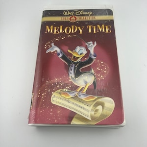 Peut inclure: Une cassette VHS Walt Disney Gold Collection du film Melody Time. La couverture montre Donald Duck en smoking dirigeant avec une baguette, debout sur un rouleau de partition musicale sur un fond rouge profond avec du texte doré et des étincelles.