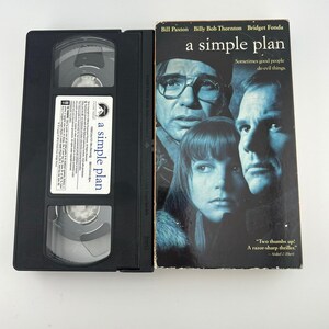 May include: A black VHS tape and its cover for the movie "A Simple Plan" are displayed. The cover features Bill Paxton, Billy Bob Thornton, and Bridget Fonda. The movie title and actors' names are visible.