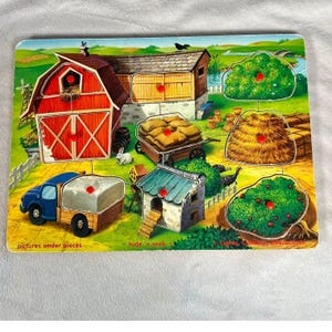 May include: A colorful wooden farm puzzle with removable pieces. The puzzle features a red barn, a blue truck, a chicken coop, and other farm elements. The puzzle has the text "pictures under pieces", "hide 'n seek", and "Lights, Games, Interaction".