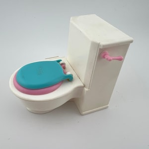 May include: A white toy toilet with a blue seat and a pink seat ring. The toilet has a pink handle and is designed for children's play. The overall design is simple and colorful.