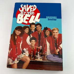 May include: A DVD box set of the TV show "Saved by the Bell" with the cast in red and white jackets. The box has a blue background with the show's logo and the text "seasons three & four".