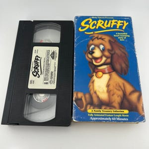 Puede incluir: Un juego de cinta VHS y caja vintage de la película animada "Scruffy". La caja presenta un perro de dibujos animados sobre un fondo azul con el título en amarillo. La cinta VHS es negra con una etiqueta blanca.
