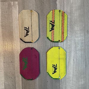 Könnte beinhalten: Vier Stoff-Patches mit den Buchstaben "WF" in Schwarz auf weißem Hintergrund. Die Patches sind in vier verschiedenen Farben: beige, gelb, grün und rosa.