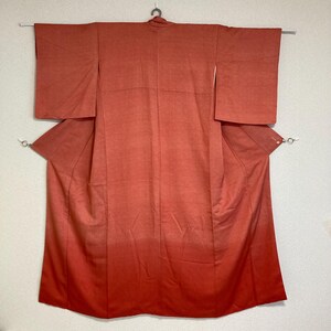 Op de afbeelding: Een traditionele Japanse kimono in een levendige oranje kleur met een verloop. De kimono is gemaakt van een gladde stof en heeft een eenvoudig ontwerp.