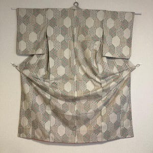 Könnte beinhalten: Ein weißer Kimono mit einem geometrischen Muster aus grünen, roten und schwarzen Punkten. Der Kimono ist gefaltet und hängt an einem Kleiderbügel.