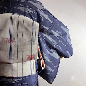 Könnte beinhalten: Ein dunkelblauer Kimono mit einem weißen Wolken- und Streifenmuster, kombiniert mit einer hellgrauen Obi-Schärpe. Der Obi ist mit dünnen vertikalen blauen Linien, einem feinen Gittermuster und kleinen roten und schwarzen Quadratmotiven verziert.