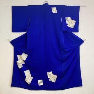 Puede incluir: Un kimono azul con patrones geométricos blancos y plateados. El kimono está doblado y se muestra sobre un fondo blanco.