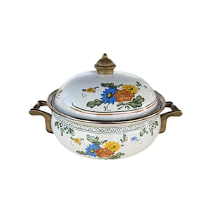 May include: White enamelware casserole dish with a lid, featuring a floral design in blue, yellow, and orange. The dish has brass-colored handles and a decorative rim. The lid is topped with a brass-colored knob.