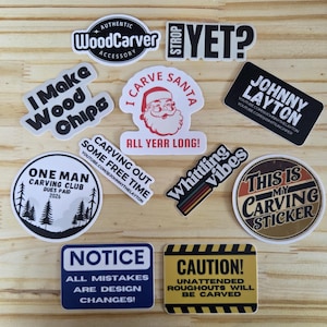 Puede incluir: Una colección de diez pegatinas de vinilo con varios temas de tallado en madera. El texto incluye "I Make Wood Chips", "I Carve Santa All Year Long", "One Man Carving Club", "Strop Yet?", "Whittling Vibes", "This Is My Carving Sticker" y señales de aviso.