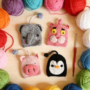 May include: A collection of handmade crochet animal keychains, including an elephant, a pink panther, a pig, and a penguin. The keychains are surrounded by colorful yarn balls and a crochet hook, showcasing the craft supplies.