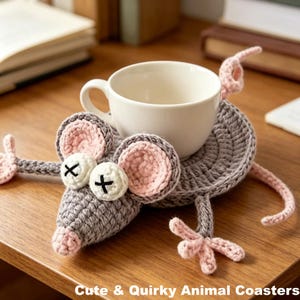May include: A gray crocheted mouse-shaped coaster with pink accents, holding a white teacup. The mouse has white eyes with black crosses, pink ears, and a pink nose. The text "Cute & Quirky Animal Coasters" is at the bottom.
