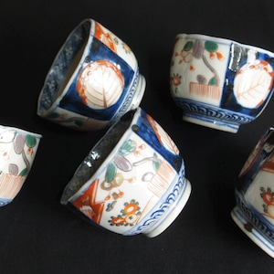 以下が含まれることがあります： 青、赤、金で描かれた花柄と幾何学模様が施された、白い磁器製の小さな湯呑みが5つ。