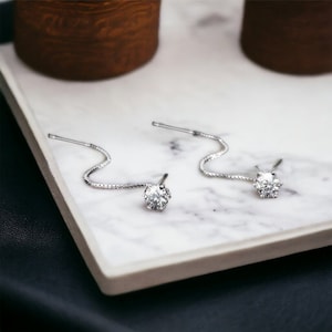 Puede incluir: Un par de pendientes de plata con un solo cristal redondo transparente en cada pendiente. Los pendientes tienen una cadena delicada que cuelga del cristal.