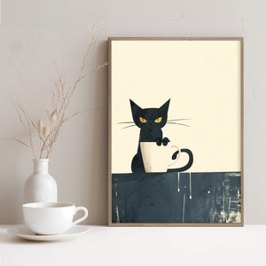 May include: A framed art print featuring a black cat with yellow eyes, perched above a white coffee cup. The cat is set against a cream background with a dark blue base. A white vase with dried stems and a white teacup are in the foreground.