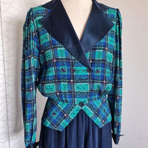 May include: A blue and green plaid dress with a black satin collar and a matching skirt. The dress has a double-breasted closure and a fitted bodice.