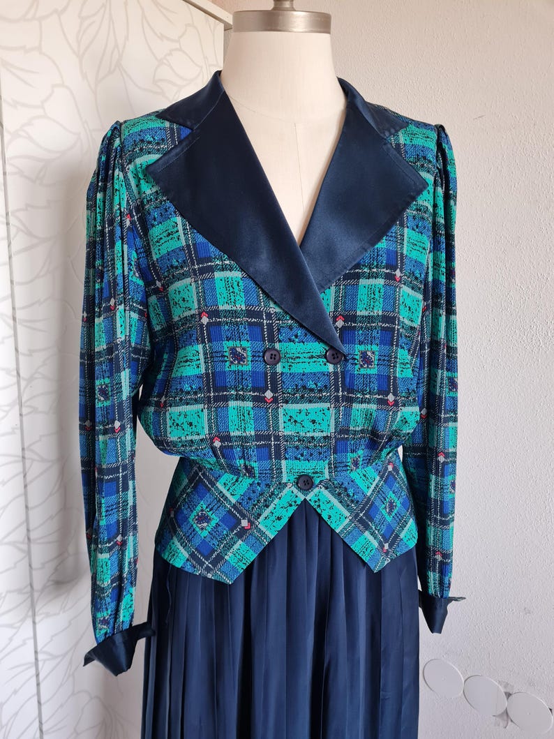 May include: A blue and green plaid dress with a black satin collar and a matching skirt. The dress has a double-breasted closure and a fitted bodice.