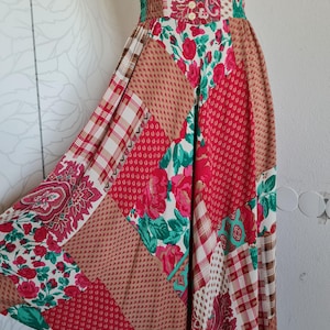 Könnte beinhalten: Ein Patchwork-Rock mit hohem Bund und fließender Silhouette. Der Rock zeigt eine Vielzahl von Mustern, darunter Blumen-, Paisley- und Karomuster in Rot-, Rosa- und Brauntönen. Der Bund ist gerafft und mit drei Knöpfen verziert.