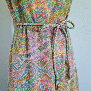 Pu&ograve; includere: Un abito vintage con stampa paisley in tonalit&agrave; rosa, verde, arancio e blu. L'abito ha una cintura con lacci e frange.