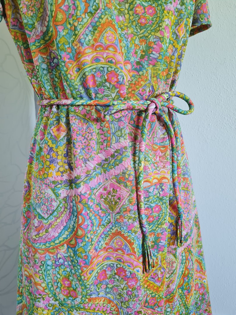 Pu&ograve; includere: Un abito vintage con stampa paisley in tonalit&agrave; rosa, verde, arancio e blu. L'abito ha una cintura con lacci e frange.