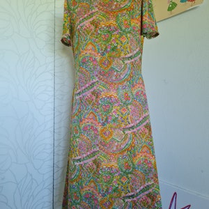 Pu&ograve; includere: Un abito vintage con collo alto e maniche corte. L'abito &egrave; realizzato in tessuto paisley colorato con sfumature di rosa, verde, arancione e giallo.
