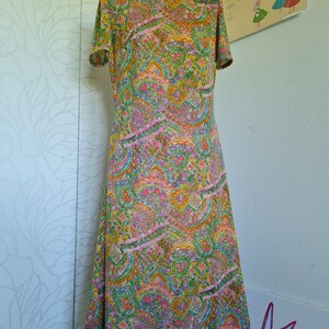 Pu&ograve; includere: Un abito vintage con stampa paisley in tonalit&agrave; di verde, rosa, arancio e giallo. L'abito ha un collo alto e maniche corte.