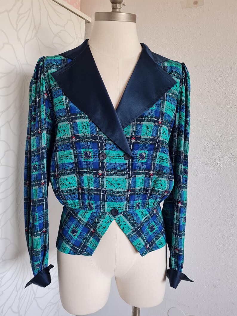 May include: A blue and green plaid blazer with a black satin collar and cuffs. The blazer has a double-breasted closure and a fitted waist.